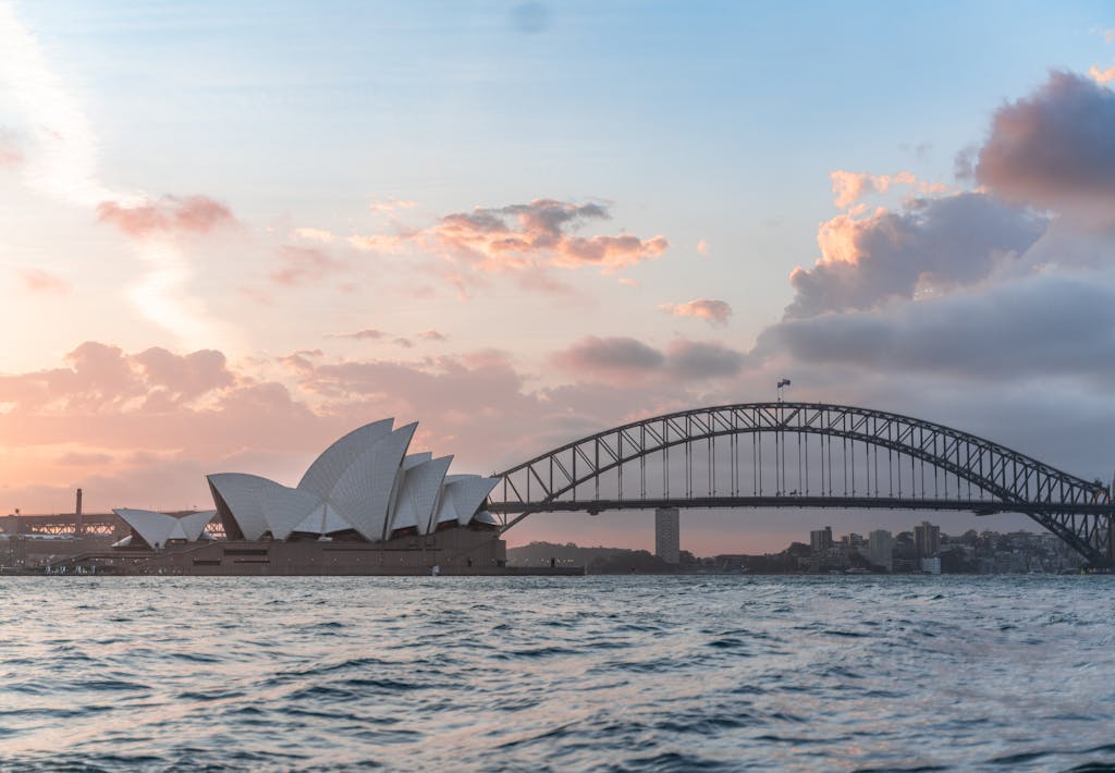 HOME Amazing cityscape of Sydney with famous Opera House and arched Harbour Bridge connecting districts against picturesque cloudy sunset sky