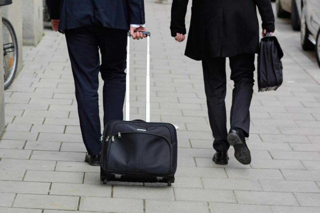 Two business professionals in suits walking on a Chicago street with luggage, showcasing urban lifestyle.