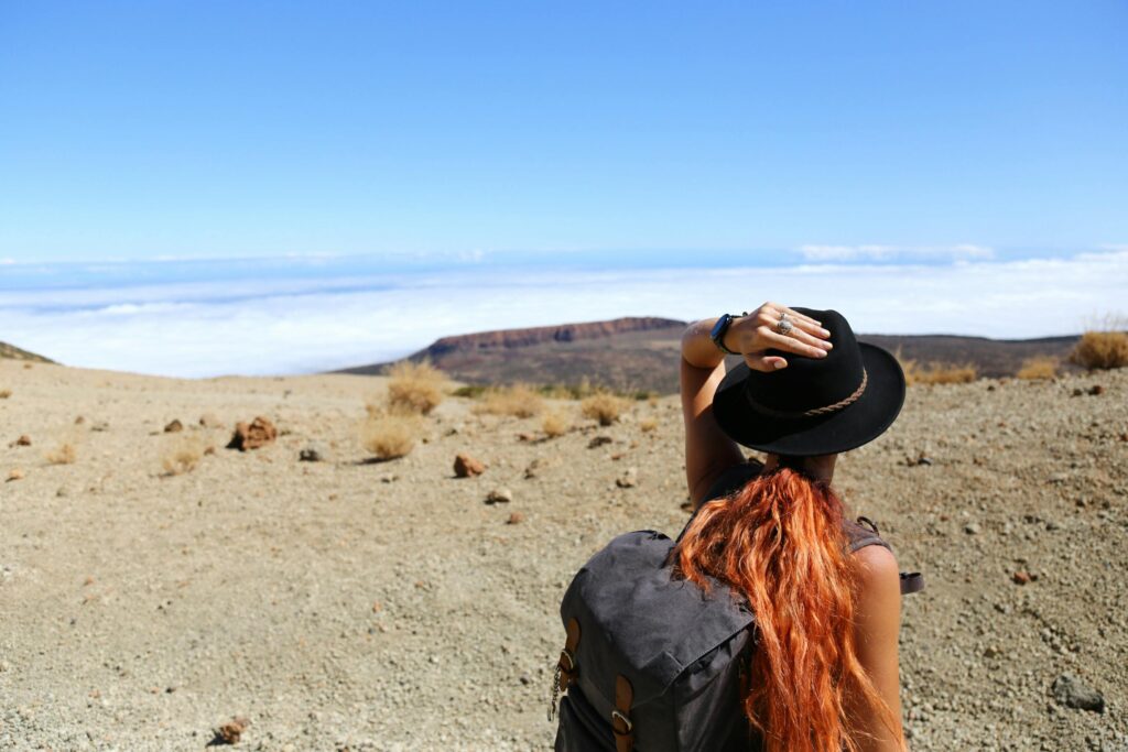 Woman standing in a desert landscape, looking at distant mountains, wearing a hat and backpack.