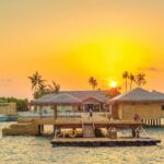 Beautiful sunset view at Kanuhura, Maldives with overwater bungalows and serene ocean surroundings.