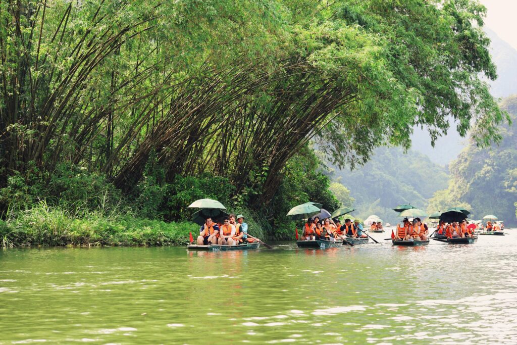 Tourists on traditional boats explore the lush waterways of Ninh Bình, Vietnam under the shade of bamboo groves.