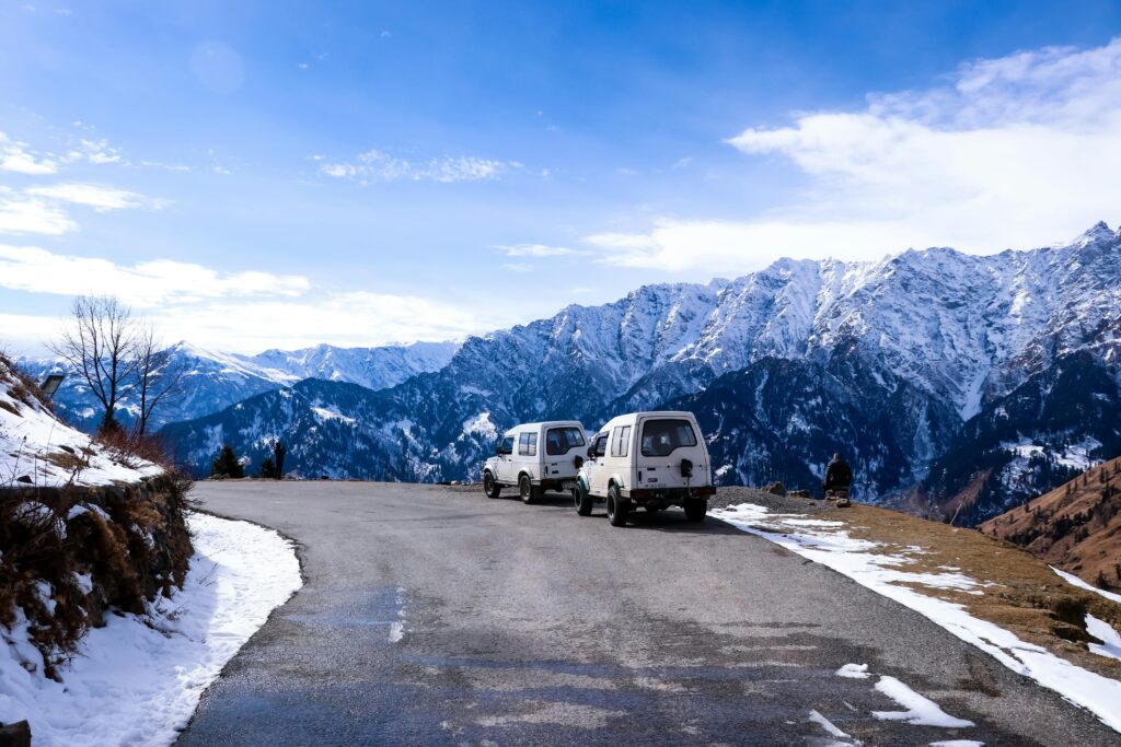 Chandigarh Shimla Manali Tour Package Idyllic winter road trip scene with vehicles and mountains in Himachal Pradesh.